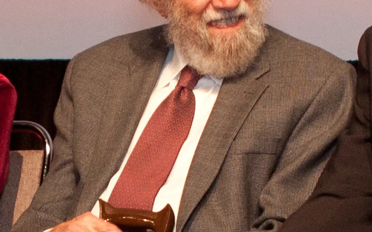 Alexander "Sasha" Shulgin, elderly, smiling, in a grey suit and red tie, holding a cane